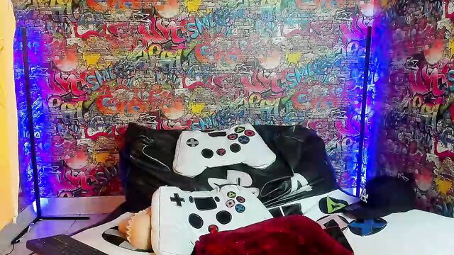 Twink gay hookup with tats, controllers on bed, colorful room vibe