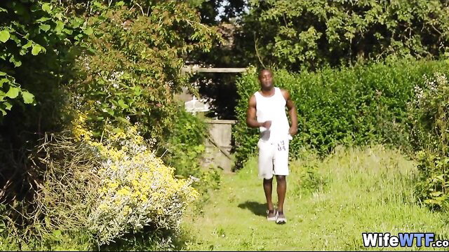 Ebony guy in white tank and shorts strolls garden path