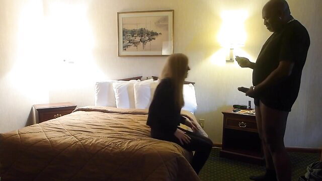 Black man naked with BBC stands over seated white blonde MILF in hotel room