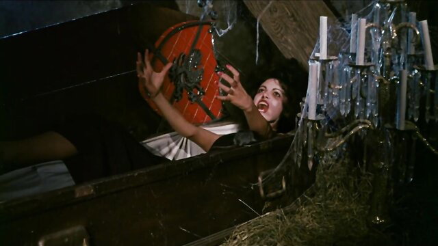 Annette Haven as vampiress clutching red shield in Dracula Sucks