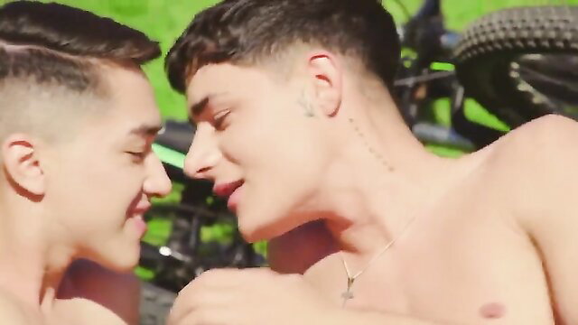 Two fit young men kissing intimately outdoors by motorcycle in summer