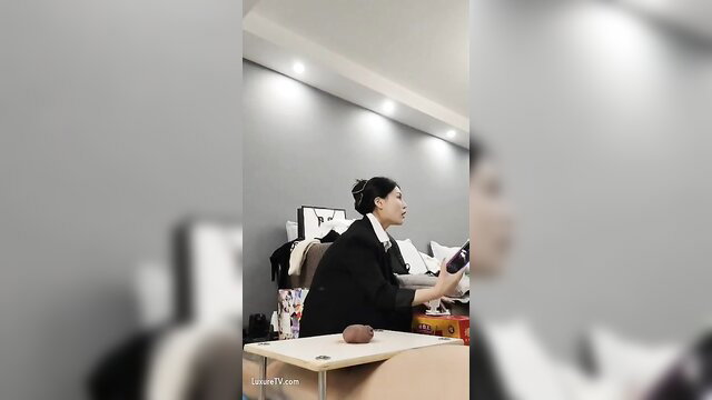 Asian femdom in black dress holds object at desk in extreme cock destruction tease