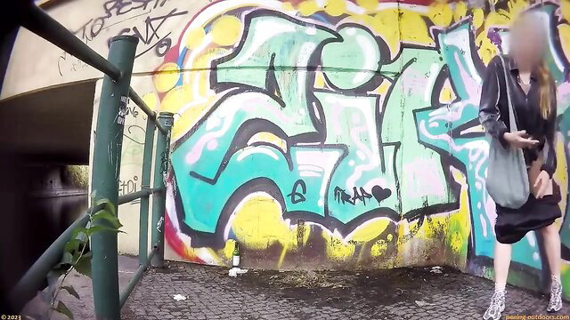 Blonde woman in dress squats to pee outdoors by graffiti wall