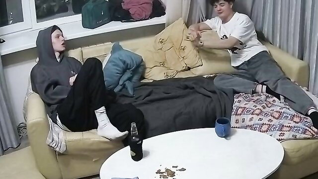 Two young white guys chilling on couch in hoodies, casual bro hangout