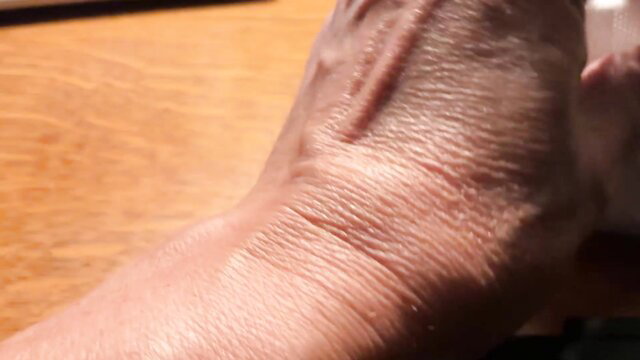 Closeup of mature woman's wrinkled hand gripping clear glass on table