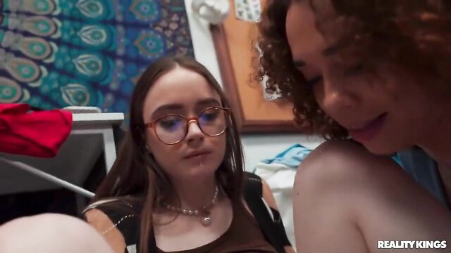 Brunette teen in glasses and curly-haired woman in dorm room tease