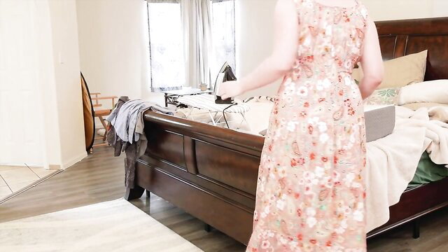 Easy going stepmom in floral dress irons clothes by bed