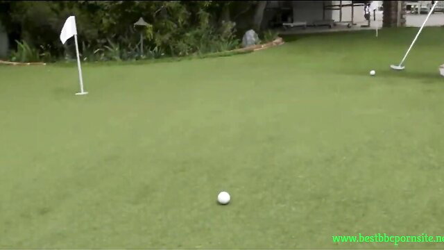 Hot chick putts golf ball on green lawn with flag in outdoor setting