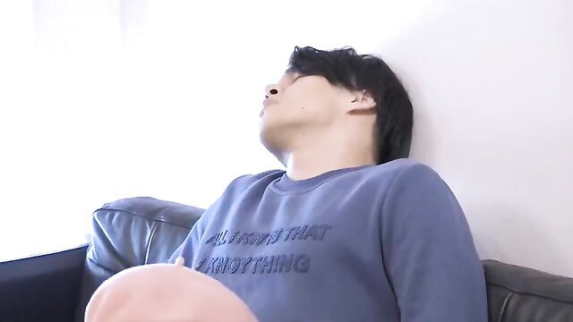 Hot Asian guy reclining on couch in tight sweater, seductive pose