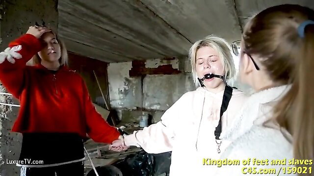 Blonde lezdom slave gagged, held by brunettes in ruined room spit play