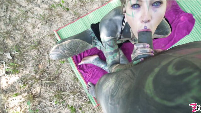 Tattooed woman sucking huge black dildo outdoors, heavy tats & makeup
