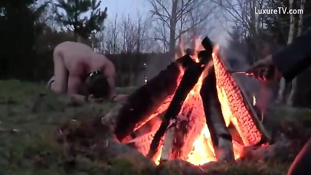 Nude woman kneeling by campfire in Danish femdom outdoor branding scene