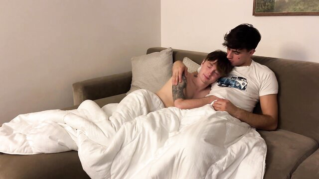 Kyle and Kam cuddling intimately under sheets on couch