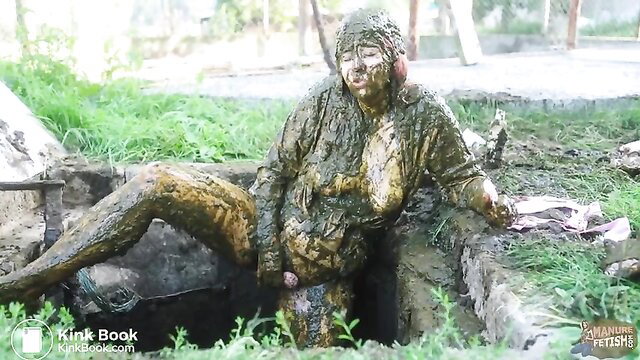 Muddy woman covered in cow shit sits legs spread in outdoor filth