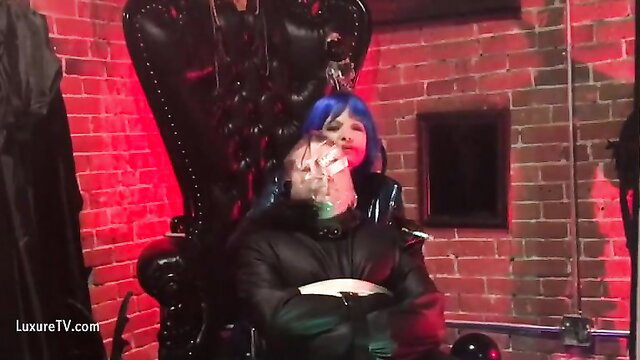 Blue-haired dominatrix tortures submissive man in latex on throne