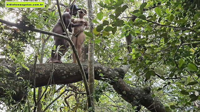Nude black tribal couple embracing on tree branch in jungle