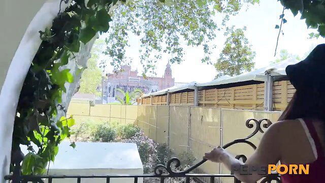 Busty European tourist babe in hat at balcony railing, Seville castle view