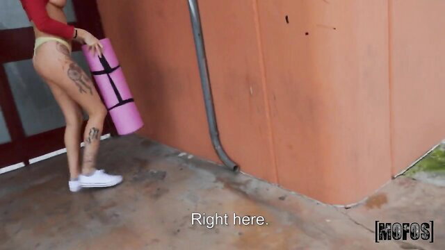 Tattooed teen in thong and crop top holding yoga mat outdoors