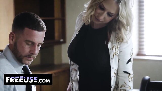 Blonde MILF in blouse and dress leans over man at office desk