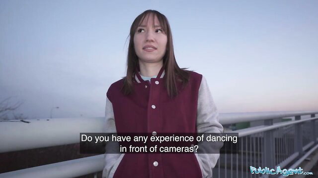 Cute Asian teen in varsity jacket asked about dancing on camera outdoors