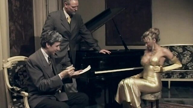 Anna Nova in gold dress at piano with suited men, Une Famille Perverse