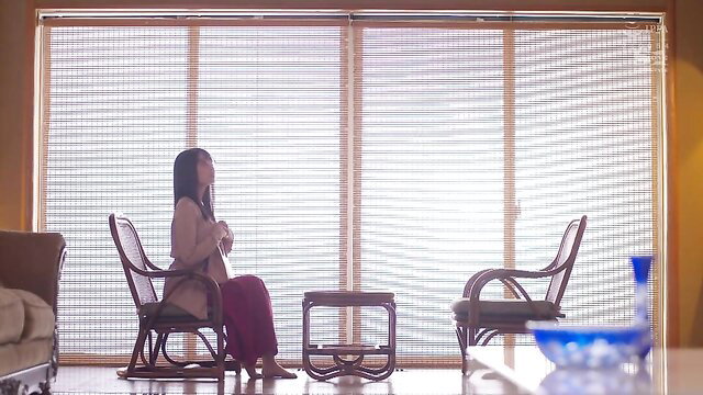 Asian beauty in pink dress sits pensively by window
