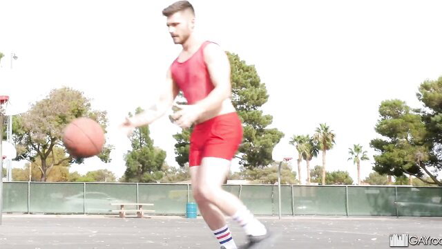 Sweaty muscular guy in tight red tank and shorts dribbles basketball after one-on-one game