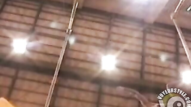 Topless gymnast performs on uneven bars in warehouse gym