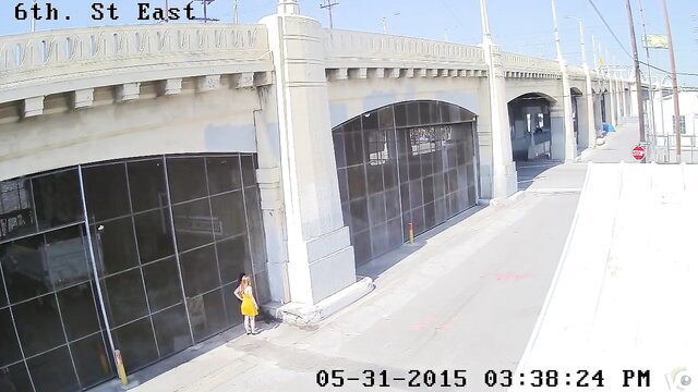 Blonde in yellow dress pees by bridge on security cam, daylight