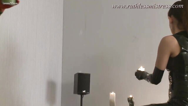 Ruthless Mistress in latex gloves holding lit candles for hot wax play