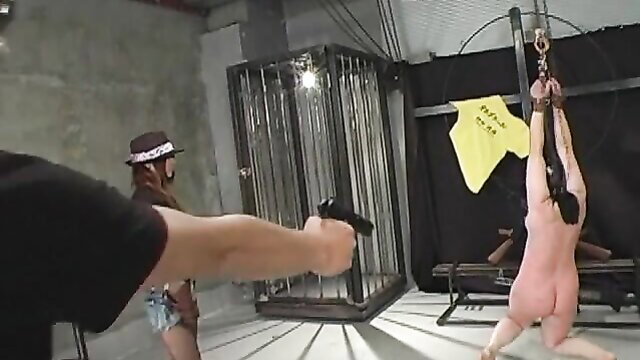 Asian domme in hat aims gun at nude bound sub in intense BDSM
