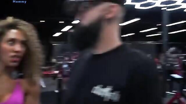 Curvy black woman in pink lingerie confronts bearded Bradley Martyn in gym