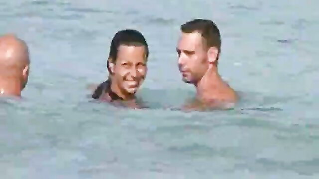 Nude brunette woman smiling with fit man in water at nudist beach