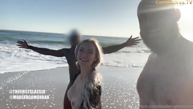 Blonde babe nude on beach with blurred black guy, arms spread in public tease