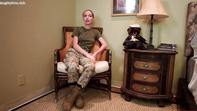 Slim white blonde in camouflage army uniform sits legs spread in bedroom