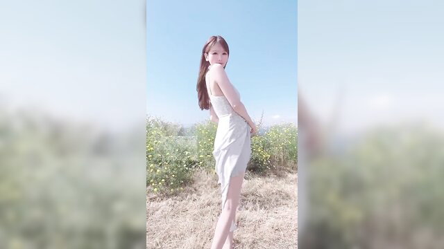Asian beauty in short white dress posing outdoors in field