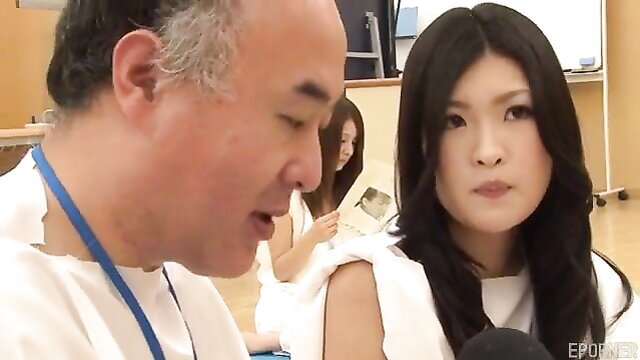 Asian JAV group with mature man talking to busty black-haired woman in white dress