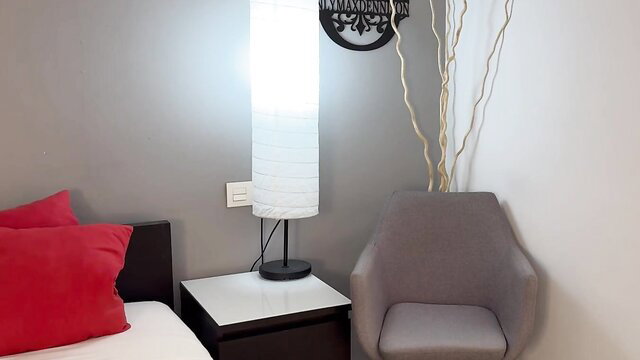 Cozy bedroom with red pillows, white lamp and gray chair