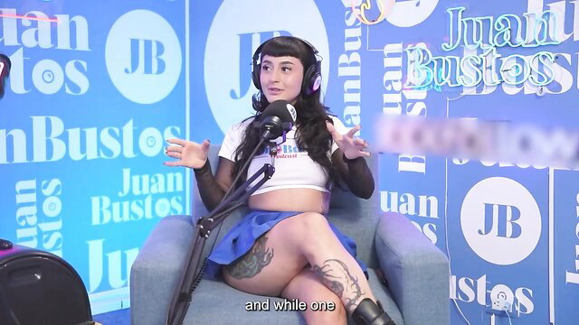 Tattooed Asian babe in white crop top and blue skirt on podcast chair