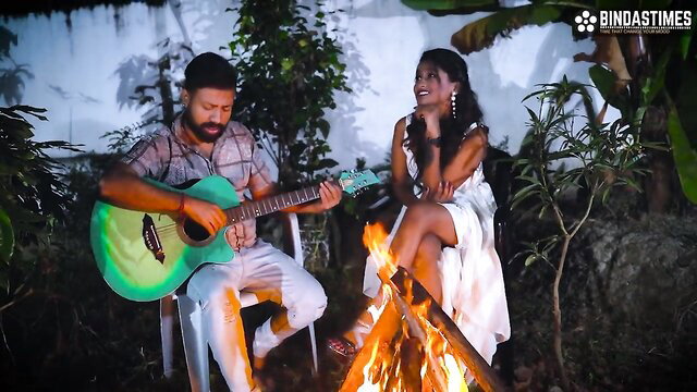StarSudipa in white dress flirts with man playing guitar by campfire outdoors