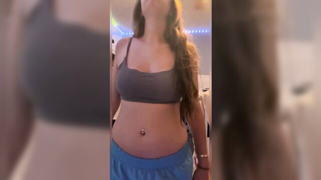 Burping blonde girl in gray sports bra and blue shorts showing navel piercing