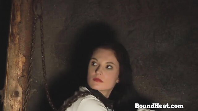 Bound brunette beauty in chains, sexy gaze in dim dungeon