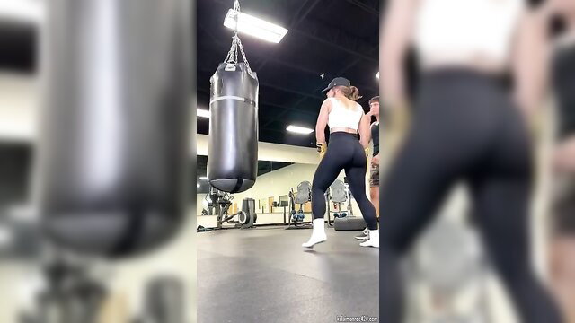 Blonde woman in tight leggings punching bag at gym, sexy workout ass view