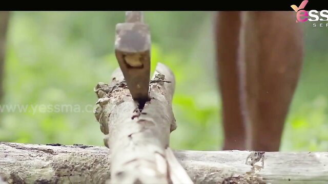 Desi woman chopping wood with axe in forest, bare legs and feet visible