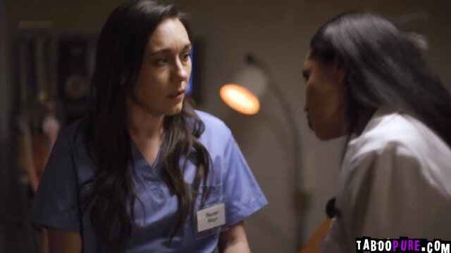 Brunette and black nurse in scrubs whispering intimately in hospital