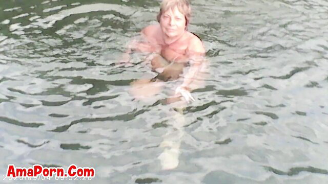 Blonde mature woman naked in clear calm waters, topless outdoor swim