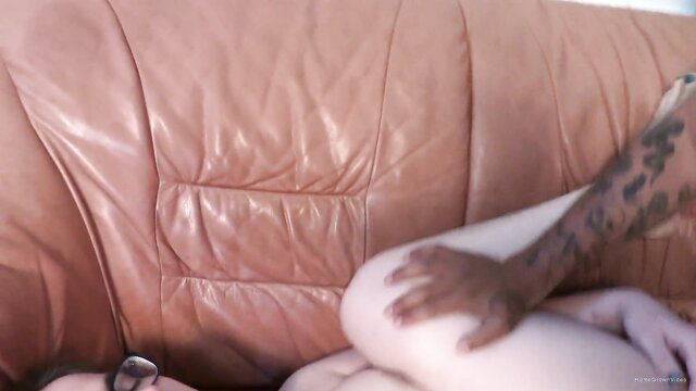 Tattooed black hand gropes pale girl's thigh on couch in amateur sex vid