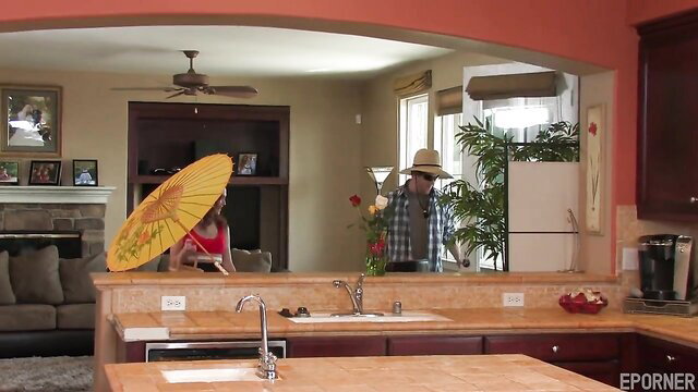 Young redhead with umbrella in kitchen teases man in hat