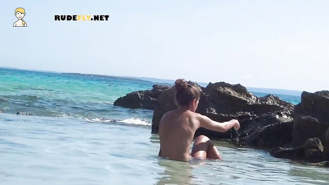 Beautiful nude teen girl sitting naked on sunny beach rocks by turquoise sea