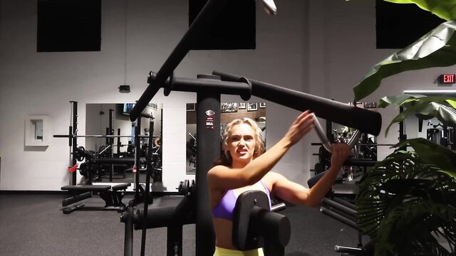 Blonde bombshell in tight sports bra flexing at gym workout